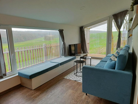 Salon moderne au Panorama Cottage Gulperberg, Pays-Bas, avec canapé bleu et vue panoramique sur la campagne.