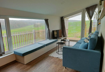 Moderne stue i Panorama Cottage på Gulperberg, Holland, med blå sofa og store vinduer til grøn udsigt.