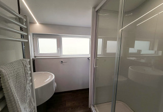 Modern bathroom with glass shower, sink, towel rail and windows at Panorama Cottage, Gulperberg, Netherlands.