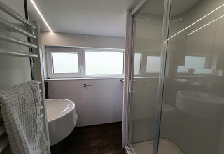 Baño moderno con ducha de vidrio, lavabo y ventanas en Panorama Cottage, Gulperberg, Países Bajos.
