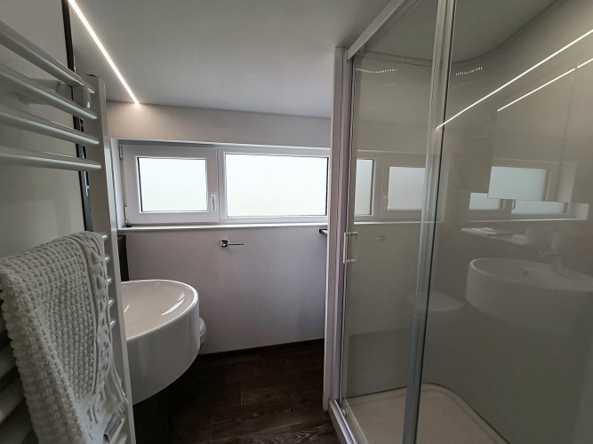 Baño moderno con ducha de vidrio, lavabo y ventanas en Panorama Cottage, Gulperberg, Países Bajos.