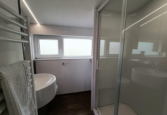 Moderne badeværelse med glasbrusekabine, håndvask og vinduer på Panorama Cottage, Gulperberg, Holland.