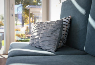 Hyggelig stue i Panorama Cottage ved Gulperberg, Holland, med blå sofa og elegante puder i sollys.