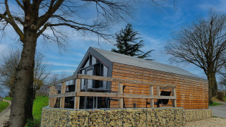 Solo Retreat lodge featuring a wooden exterior, stone foundation, deck area, trees and a bright blue sky.