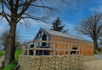 Solo Retreat lodge met houten gevel, stenen fundering, terras, omringd door bomen en blauwe lucht.