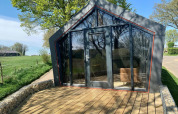 Et moderne Solo Retreat-lodge i Gulperberg, Holland, med glasfacade og træterrasse under træer.
