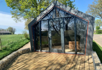 Moderne Solo Retreat-lodge op Gulperberg, Nederland, met glazen voorgevel en houten terras buiten.