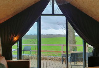 Zicht vanuit Solo Retreat bij Gulperberg in Nederland, over groene velden via grote glazen ramen.