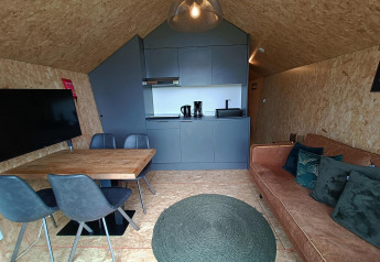 Moderne indretning med køkken, spisebord, sofa og tv i Solo Retreat lodge på Gulperberg, Holland.