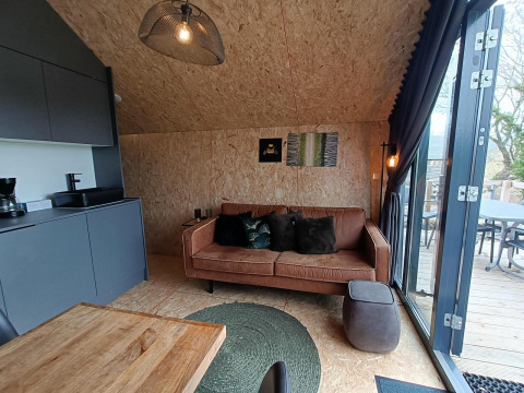 Interior moderno de cabaña con sofá marrón y puertas de cristal en Solo Retreat en Gulperberg, Países Bajos.