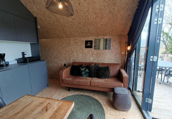 Interno di lodge moderno con divano marrone e porte in vetro al Solo Retreat, Gulperberg, Paesi Bassi.