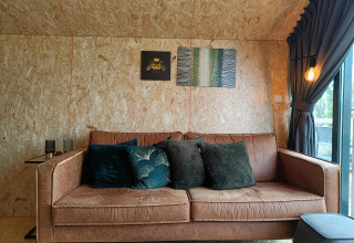 Knusse bruine sofa met sierkussens in Solo Retreat lodge aan Gulperberg, Nederland, en wanddecoratie.