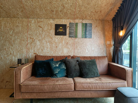 Sofá marrón cómodo con cojines en el lodge Solo Retreat en Gulperberg, Países Bajos, y arte en la pared.