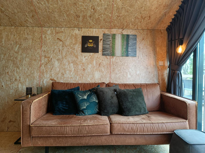 Sofá marrón cómodo con cojines en el lodge Solo Retreat en Gulperberg, Países Bajos, y arte en la pared.