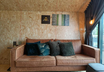 Comfortabele bruine bank met sierkussens in Solo Retreat lodge op Gulperberg, Nederland, met wanddecoratie.