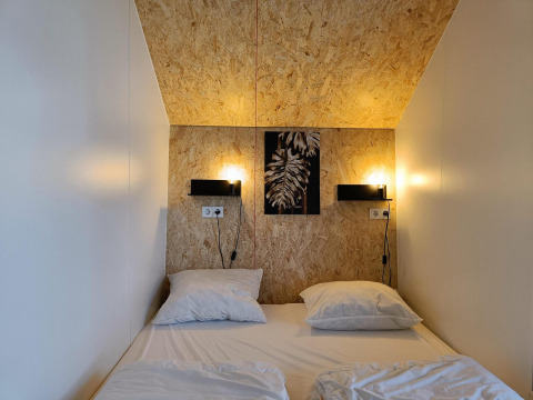 En hyggelig seng med to puder i Solo Retreat-lodgen ved Gulperberg, Holland, med varm belysning.
