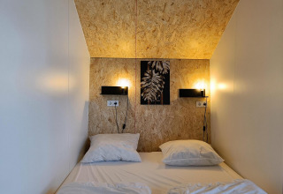 En hyggelig seng med to puder i Solo Retreat-lodgen ved Gulperberg, Holland, med varm belysning.