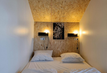 En hyggelig seng med to puder i Solo Retreat-lodgen ved Gulperberg, Holland, med varm belysning.