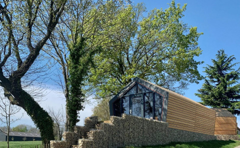 Moderna baita in legno su un muro di pietra tra gli alberi, Solo Retreat Gulperberg, Paesi Bassi, giornata serena.