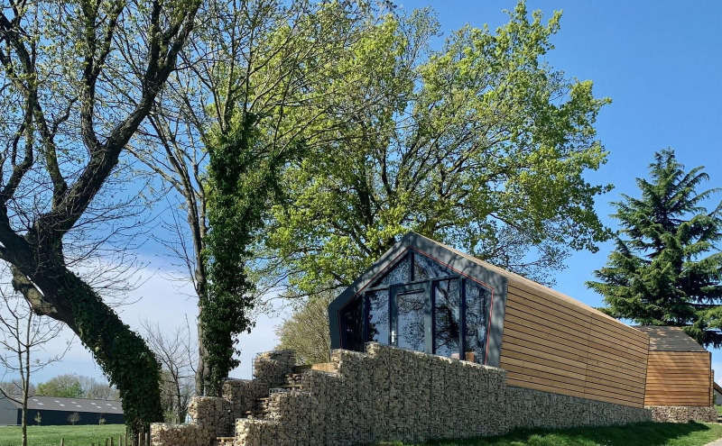 Cabaña moderna de madera sobre muro de piedra en Solo Retreat Gulperberg, Países Bajos, rodeada de árboles.