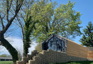 Moderne houten lodge op een stenen muur tussen bomen bij Solo Retreat Gulperberg, Nederland, zonnige dag.