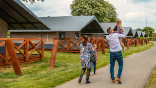Een gezin loopt langs glampingtenten met houten terrassen op een verzorgde camping tussen de bomen.