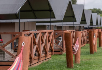 Rij lodges met houten terrassen en hangmatten op het gras, genomen op een lodge onder bewolkte hemel.