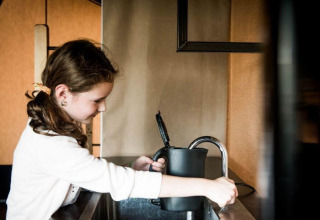 Mädchen füllt einen Wasserkocher am Wasserhahn in einer modernen Glamping-Unterkunft mit Wasser.