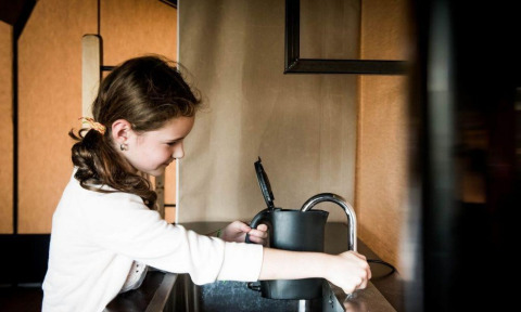 Fille remplissant une bouilloire d'eau au robinet dans une cuisine intérieure d’hébergement glamping moderne.