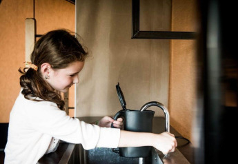 Fille remplissant une bouilloire d'eau au robinet dans une cuisine intérieure d’hébergement glamping moderne.