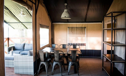Vista interior de una tienda espaciosa con mesa de comedor, sillas y sofá en Panorama Lodge, Gulperberg, Países Bajos.