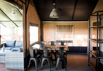 Vue intérieure d'une tente spacieuse avec table à manger, chaises et canapé à Panorama Lodge, Gulperberg, Pays-Bas.
