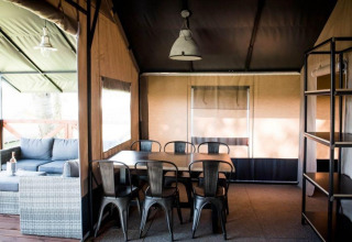 Vista interna di una spaziosa tenda con tavolo da pranzo, sedie e divano al Panorama Lodge, Gulperberg, Paesi Bassi.