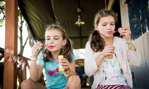 Due bambine soffiano bolle di sapone sulla veranda di Panorama Lodge a Gulperberg, Paesi Bassi, felici.