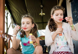 Due bambine soffiano bolle di sapone sulla veranda di Panorama Lodge a Gulperberg, Paesi Bassi, felici.