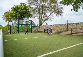 Famille jouant au football sur un terrain de sport extérieur avec panier de basket dans un site de glamping.