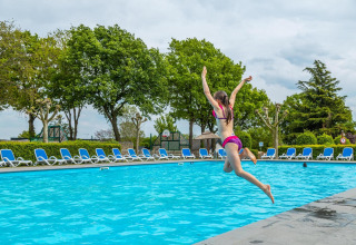 Una ragazza salta in piscina in una sistemazione glamping, circondata da lettini e alberi verdi.
