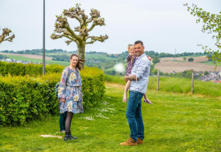 Famiglia che si gode una vacanza in glamping, circondata da prati verdi e colline sullo sfondo.