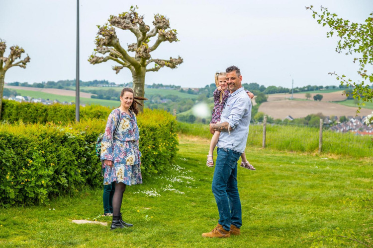 Family enjoying a scenic glamping getaway, standing on grassy field with hills and trees in the background.