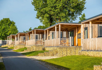 Rij moderne houten lodges met veranda’s op stenen fundering, in een groene omgeving bij Berghem Lodge.
