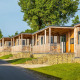Række af moderne træhytter med verandaer på stenfundament, omgivet af grønne områder i Berghem Lodge.