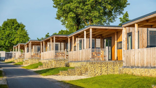 Fila de modernas cabañas de madera con porches sobre bases de piedra en un entorno verde en Berghem Lodge.
