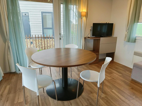 Coin repas avec table ronde, quatre chaises blanches et une télévision dans un lodge à Berghem, Gulperberg, Pays-Bas.