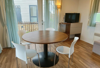 Coin repas avec table ronde, quatre chaises blanches et une télévision dans un lodge à Berghem, Gulperberg, Pays-Bas.