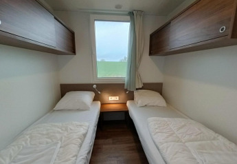 Moderne lodgekamer op Gulperberg, Nederland, met twee enkele bedden, een raam en houten kasten.