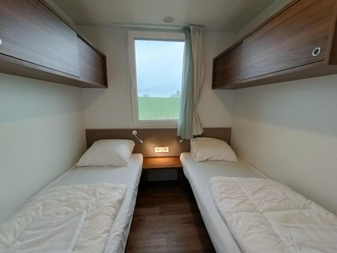 Habitación moderna de lodge en Gulperberg, Países Bajos, dos camas individuales, ventana y armarios de madera.