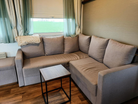 Canapé d'angle confortable dans un lodge moderne avec vue verte et rideaux clairs à Berghem at Gulperberg.