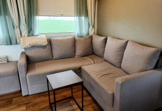 Canapé d'angle confortable dans un lodge moderne avec vue verte et rideaux clairs à Berghem at Gulperberg.