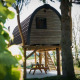 Et lille trælodgehus placeret blandt træer på Gulperberg i Holland, omgivet af grønne planter og natur.