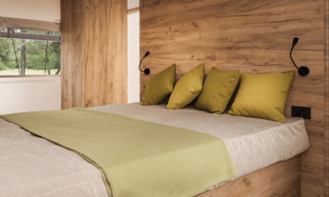 Cama acogedora con cojines verdes y pared de madera en Lodge de Montagne Petite, Gulperberg, Países Bajos.